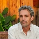Man sitting in front of a fence background in a white shirt.