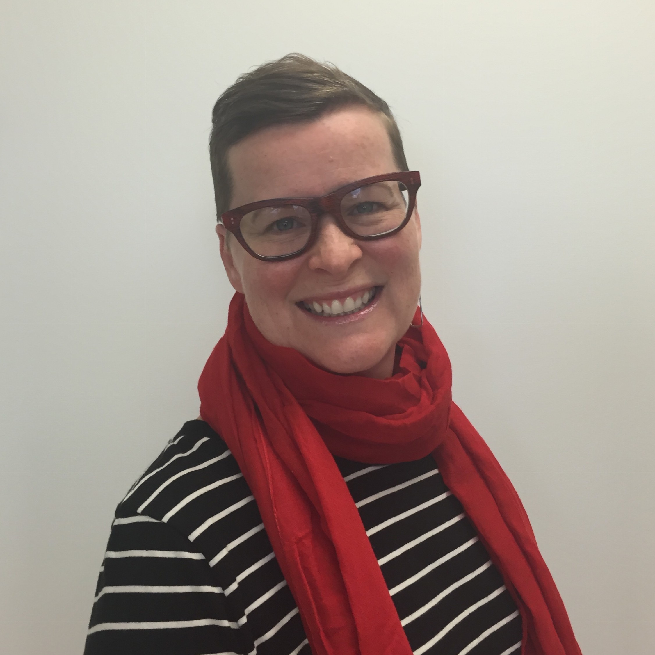 Headshot de una mujer sonriente con el pelo corto castaño y un pañuelo rojo y gafas sobre un fondo blanco
