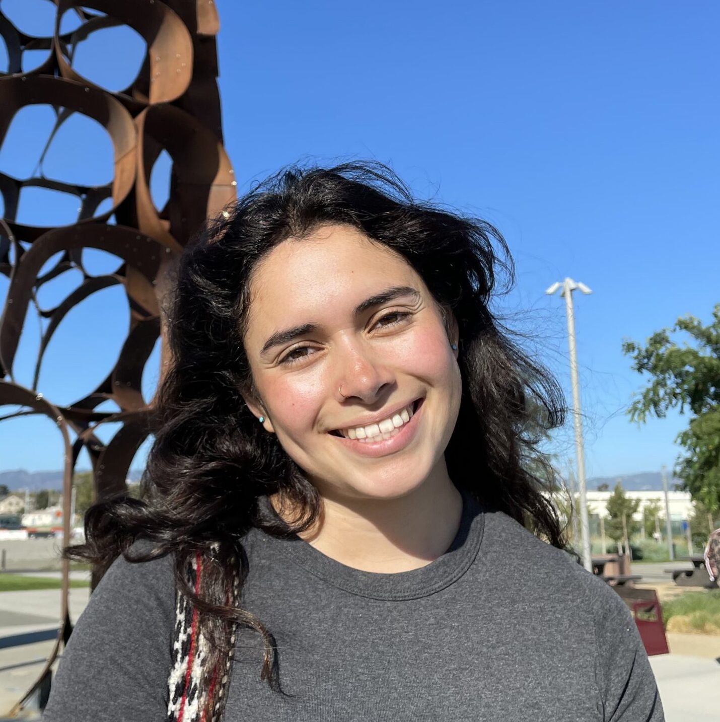 Young woman standing in front of art piece with a grey shirt and brown hair.