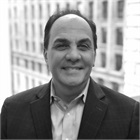 Black and white photo of a man in a suit smiling with a background of tall office buildings.