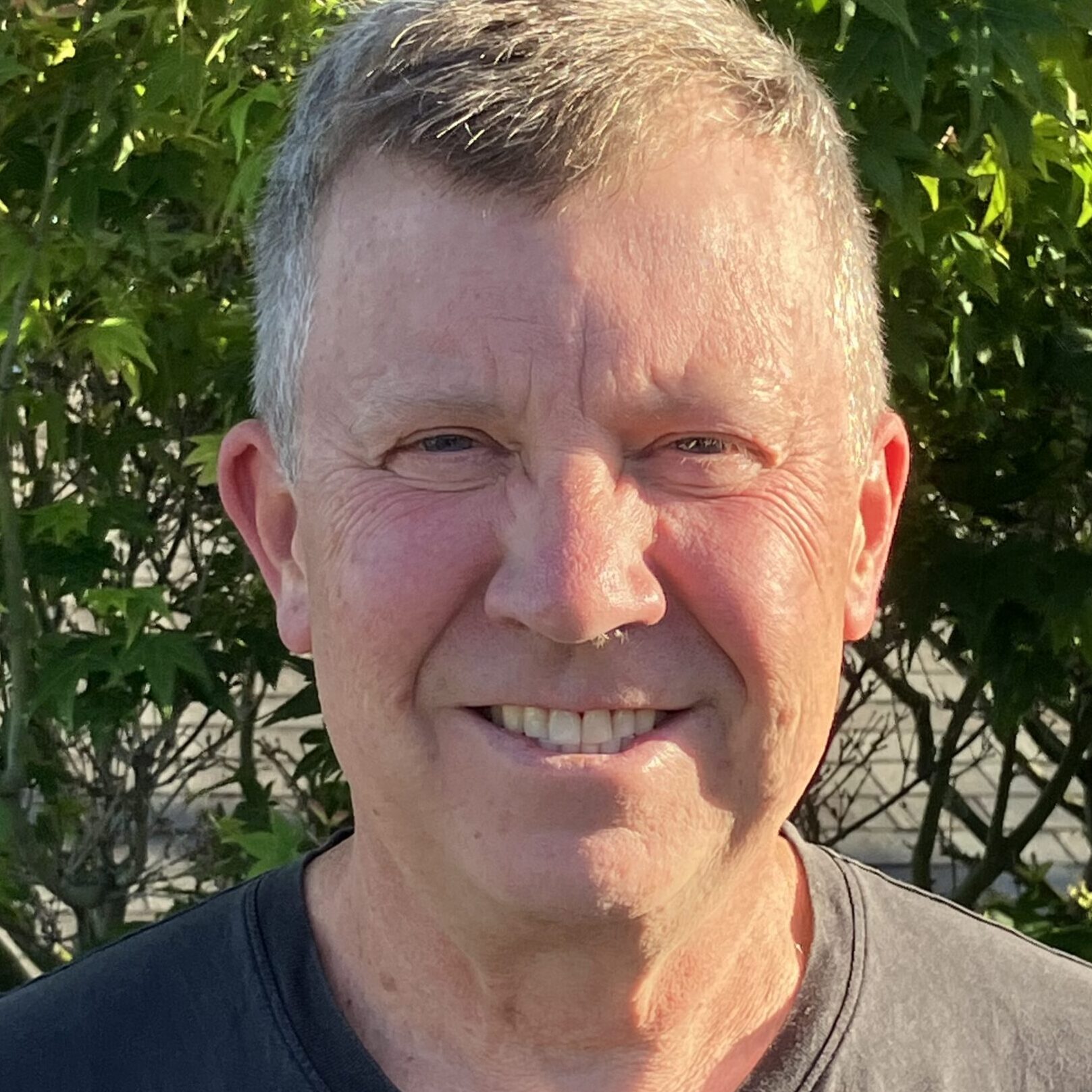 A smiling person wearing a black shirt in front of foliage