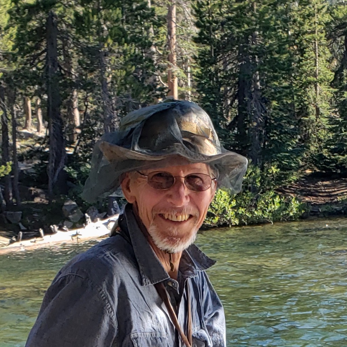 Hombre sonriente frente a un río verde y un bosque