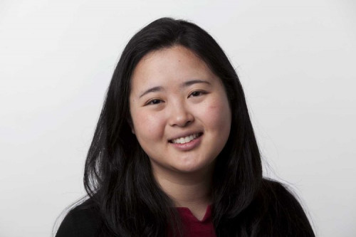Woman with dark hair and shirt in front of white background.